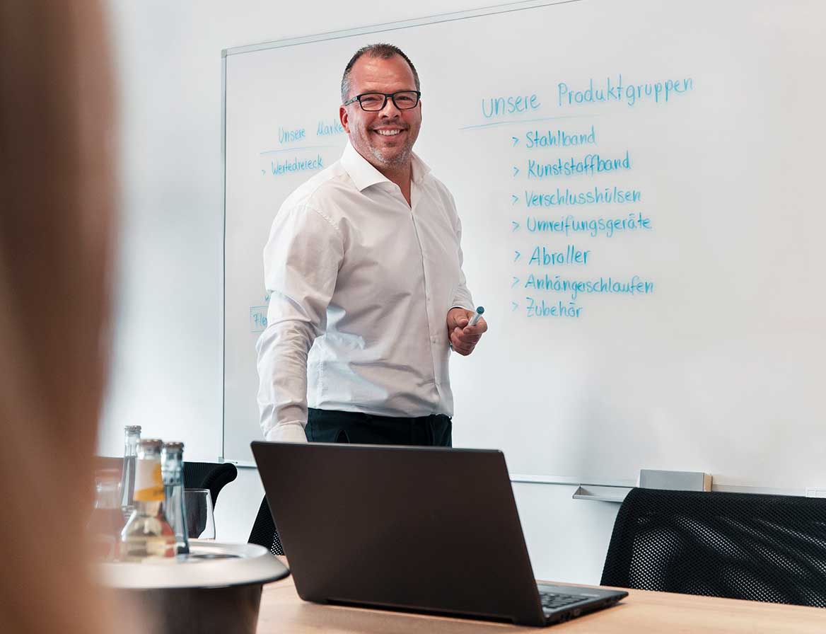 H&B Mitarbeiter steht vor einem beschrifteten Whiteboard